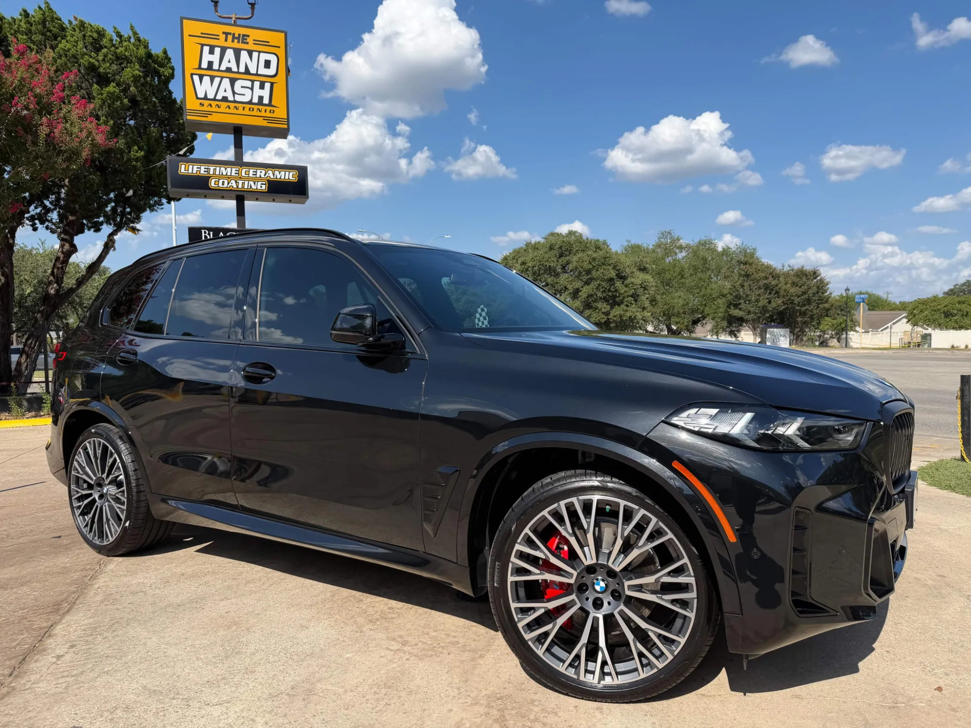 Clean black BMW SUV beside The Hand Wash San Antonio sign