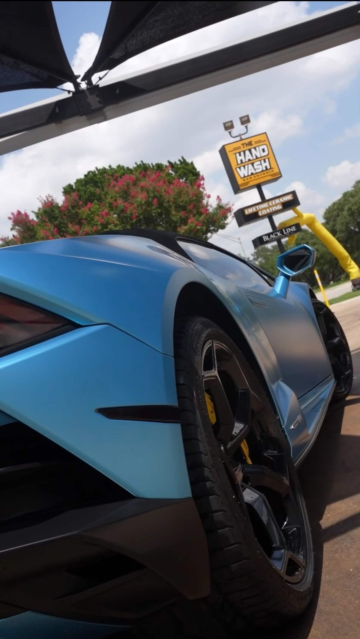 Light blue Lamborghini and The Hand Wash sign viewed from a low angle