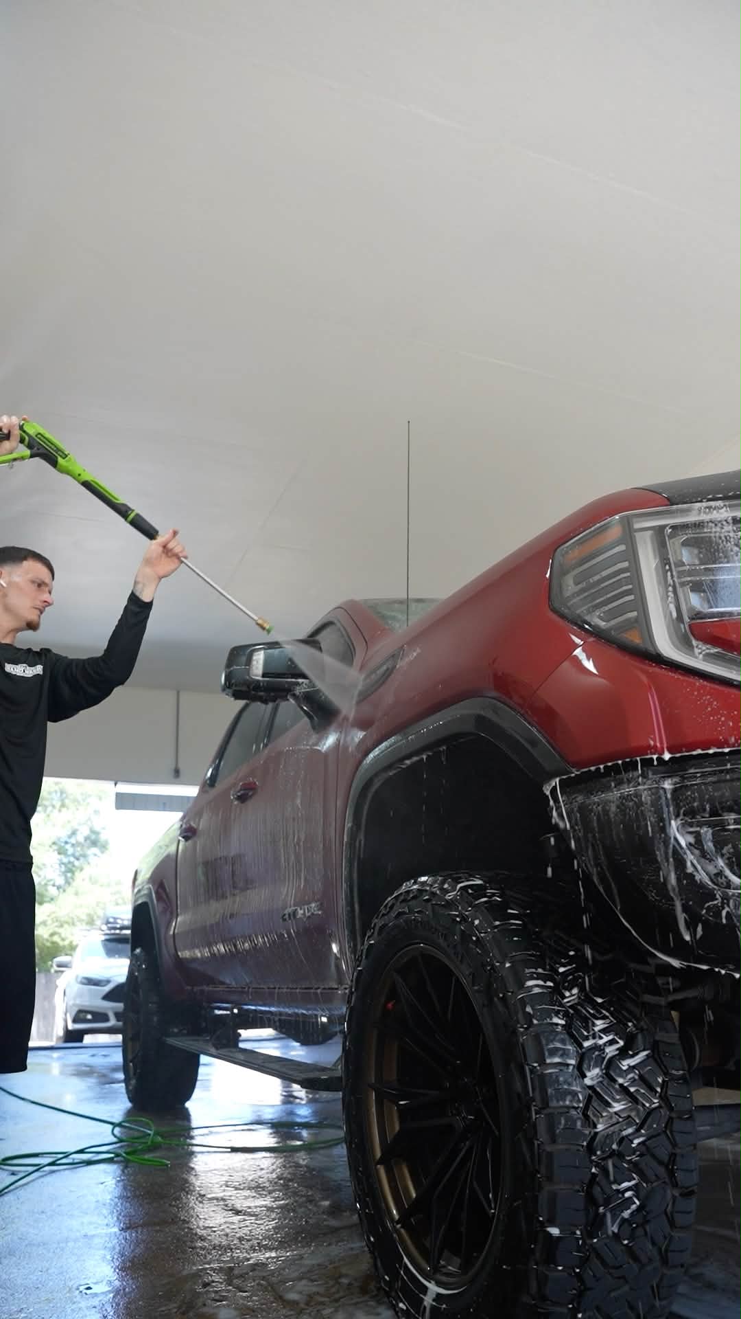 Team member pressure washing a red pickup truck in the wash bay