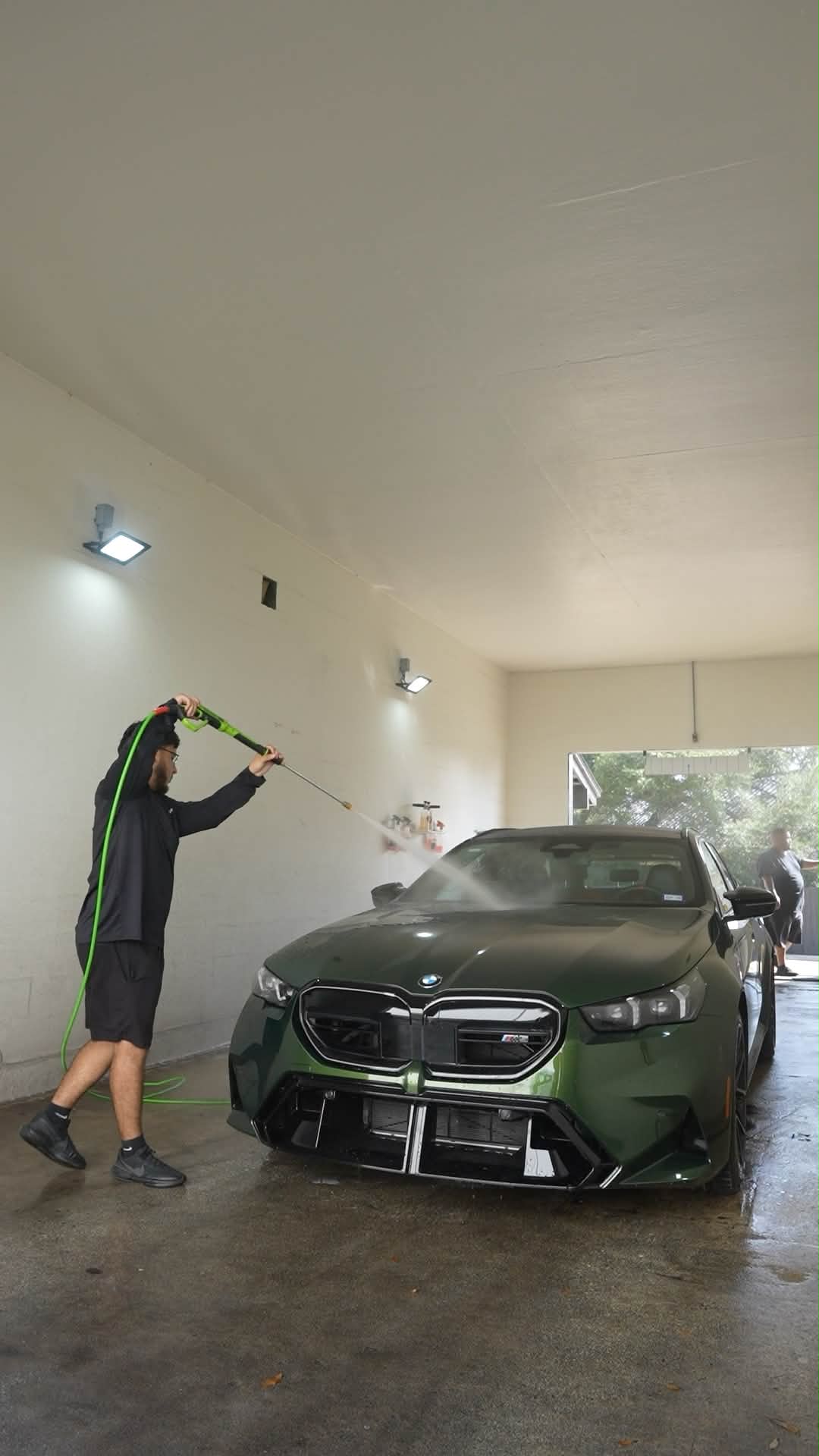 Team member pressure washing a dark green BMW in the shop
